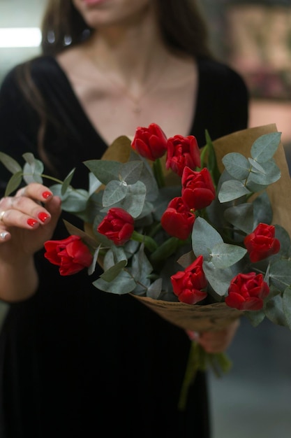 Garota desfocada com um buquê de tulipas vermelhas e eucalipto