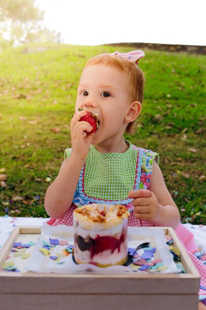 Garota desfrutando de torta de morango no parque durante um piquenique em família