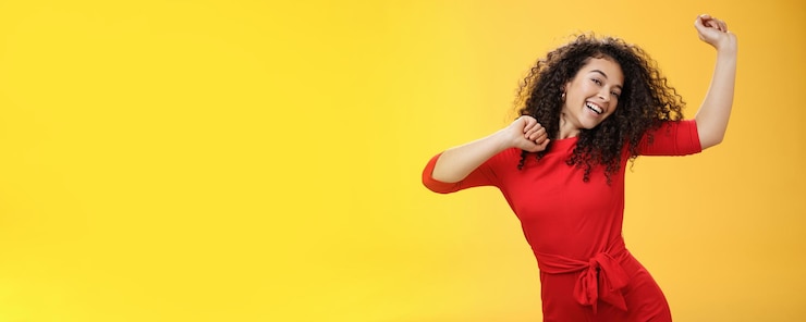 Foto garota despreocupada se sentindo animada e alegre dançando em vestido vermelho levantando as mãos alegremente inclinando a cabeça