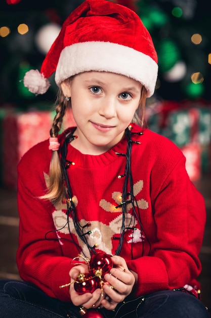 Garota do Papai Noel embrulhada em guirlanda segurando brinquedos de árvore de Natal