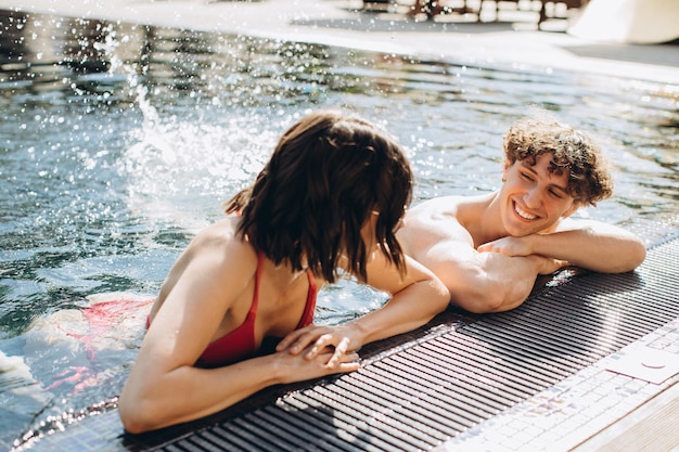 Garota e cara bonito positivo se divertem no verão à beira da piscina