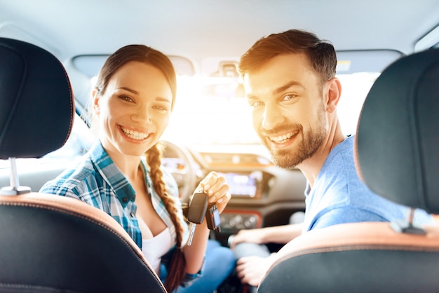 Garota e o cara estão sentados em um carro novo e sorrindo.