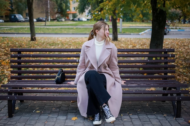 Garota elegante de casaco senta-se em um banco na cidade e sonha