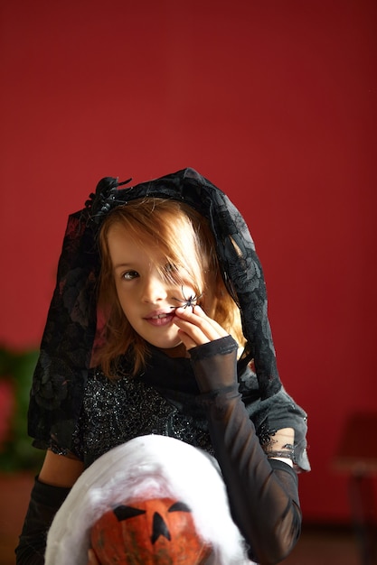 Garota em casa com fantasia de halloween com abóbora jack ou laurent nas mãos, criança usando máscara preta protegendo contra coronavírus, halloween em quarentena