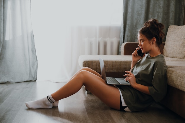Garota em casa olhando para o laptop e falando ao telefone
