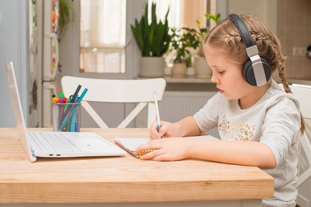 Garota em fones de ouvido faz videochamada usando notebook escrevendo notas aprendendo matéria escolar à distância