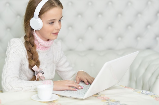 Garota em fones de ouvido usando laptop em casa