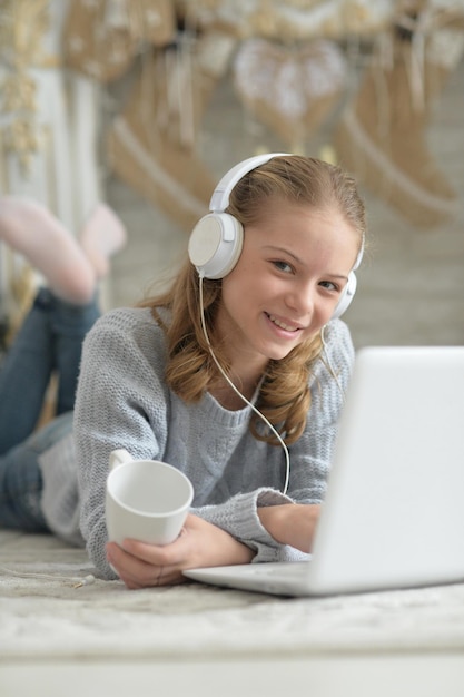 Garota em fones de ouvido usando laptop enquanto estava deitado no chão