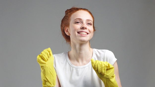 Garota em luvas de limpeza amarelas em uma parede cinza