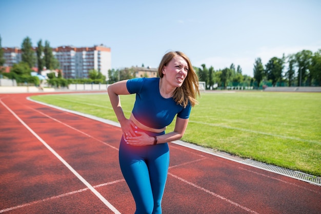 Foto garota em roupas esportivas no estádio está exausta e tem dor durante o treinamento e treino mulher esportiva tem dor de estômago esportes ao ar livre e conceito de dor