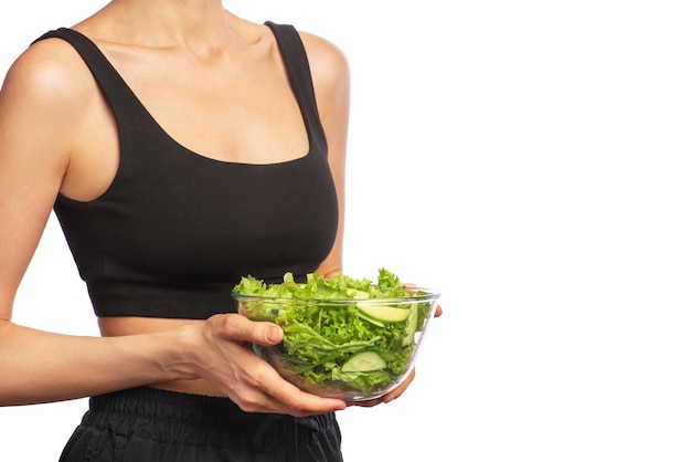 Garota em roupas esportivas pretas com uma tigela de salada verde nas mãos em um branco isolado