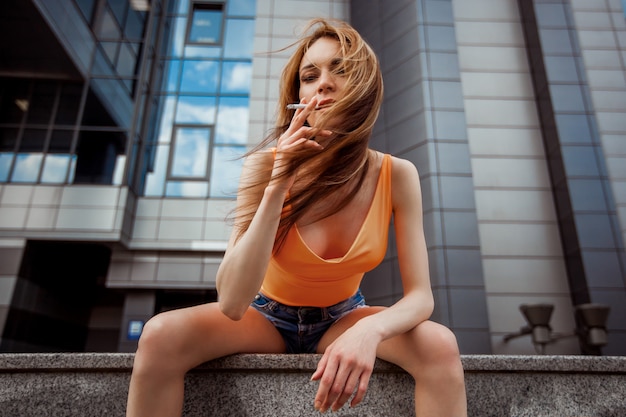 Garota em shorts, fumando na rua.