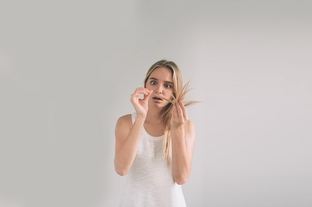 Garota em um fundo branco com um problema de cabelo. a mulher loura está vestindo a camisa isolada no branco.