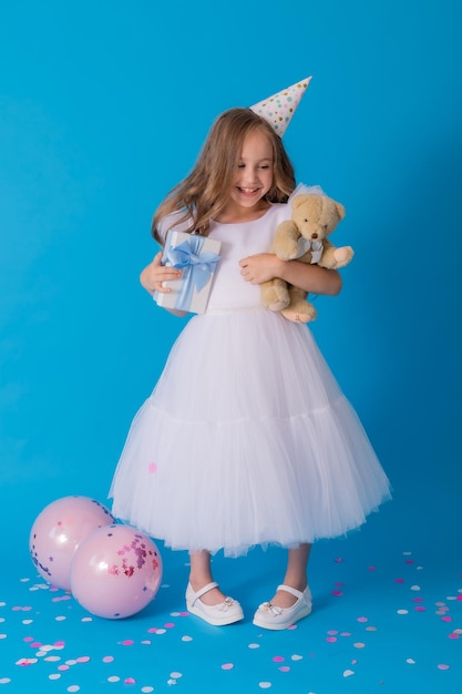 garota em um lindo vestido branco fofo tem um ursinho de pelúcia e uma caixa de presente nas mãos