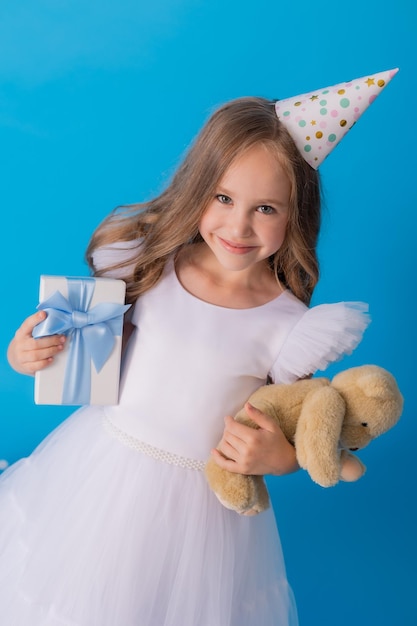 garota em um lindo vestido branco fofo tem um ursinho de pelúcia e uma caixa de presente nas mãos