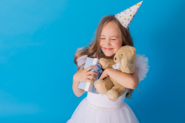 garota em um lindo vestido branco fofo tem um ursinho de pelúcia e uma caixa de presente nas mãos