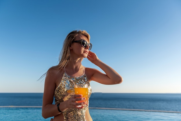 Garota em um maiô caro com um coquetel nas mãos passa as férias perto da piscina no resort