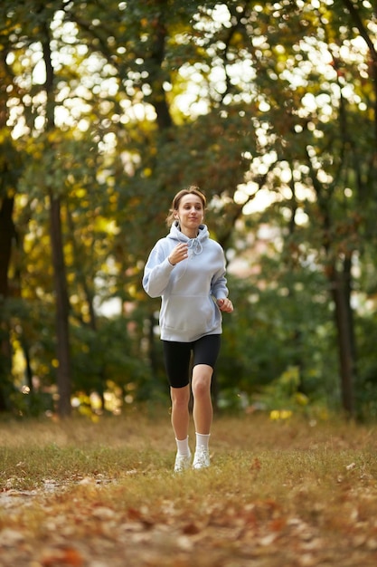 garota em um moletom azul e fones de ouvido no parque e começando a correr. garota correndo no parque.