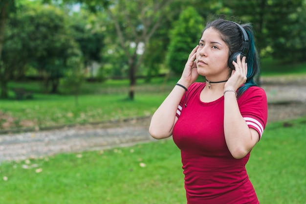 garota em um parque ouvindo música, segurando os fones de ouvido com as mãos, muito focada nas músicas.