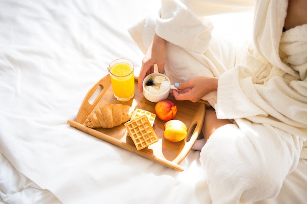 Garota em um roupão tomando café da manhã na cama