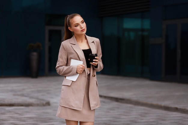 Garota em um terno de escritório com uma xícara de café e papéis no verão fora do escritório