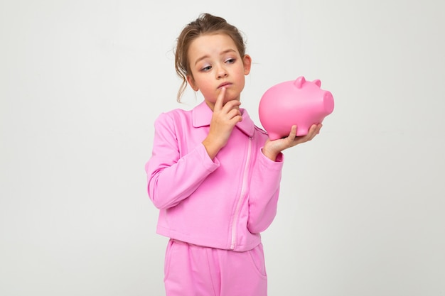 garota em um terno rosa, segurando um pote de dinheiro em uma parede branca com espaço em branco