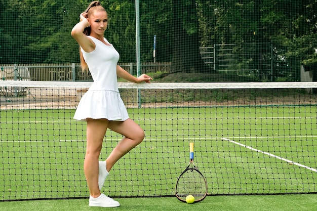Garota em um vestido branco esportivo na quadra de tênis e raquete