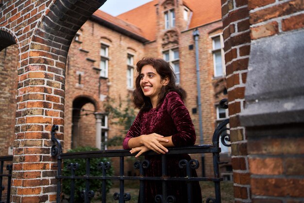 Foto garota em um vestido de cordel vermelho com as costas abertas caminha pelas ruas de bruges em um outono