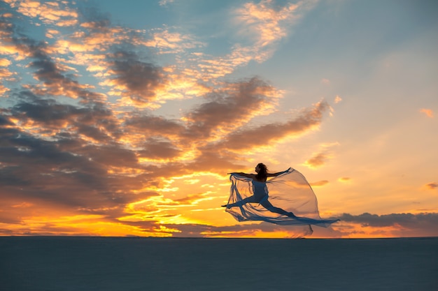 Garota em um vestido de mosca branca dança e posa no deserto de areia ao pôr do sol