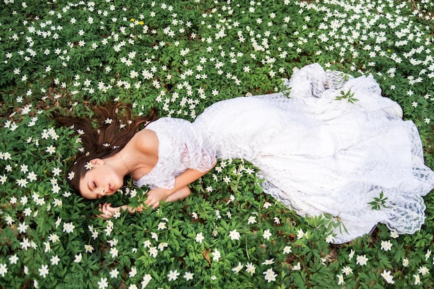 Garota em um vestido de renda branca está em uma clareira com prímulas uma jovem de cabelo comprido está dormindo em uma floresta de primavera