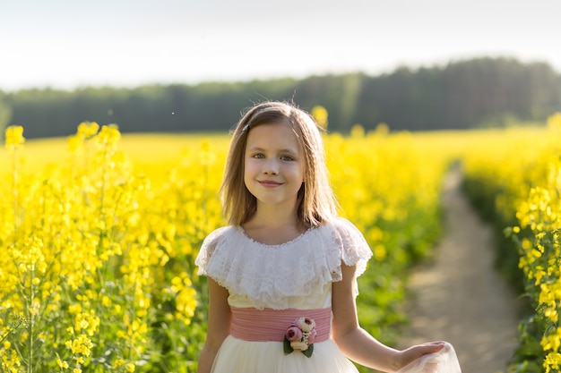 garota em um vestido longo branco em um campo de colza no verão