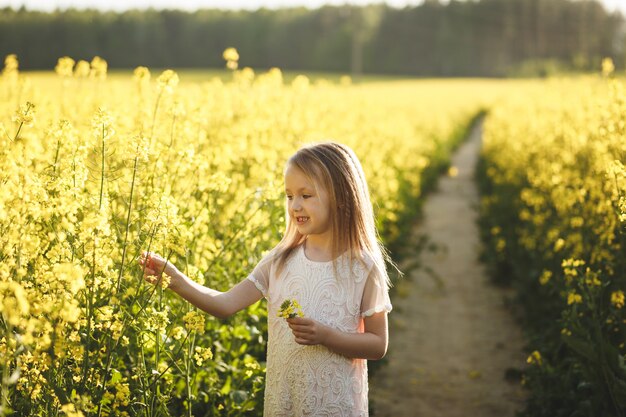 garota em um vestido longo branco em um campo de colza no verão