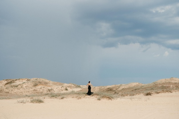 Garota em um vestido longo preto em um deserto arenoso