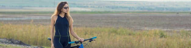 Garota em uma bicicleta de montanha em offroad belo retrato de um ciclista ao pôr do sol Garota fitness monta uma moderna bicicleta de montanha de fibra de carbono em roupas esportivas Closeup retrato de uma garota em um capacete e óculos