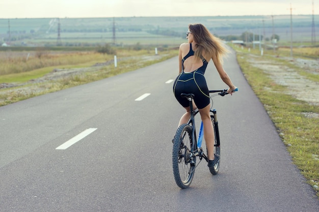 Garota em uma bicicleta de montanha em offroad belo retrato de um ciclista ao pôr do sol Garota fitness monta uma moderna bicicleta de montanha de fibra de carbono em roupas esportivas