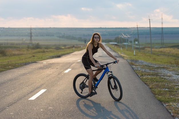 Garota em uma bicicleta de montanha em offroad belo retrato de um ciclista ao pôr do sol Garota fitness monta uma moderna bicicleta de montanha de fibra de carbono em roupas esportivas