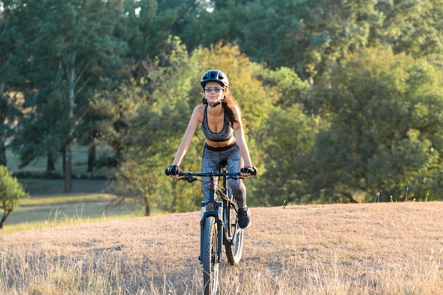 Garota em uma bicicleta de montanha em offroad belo retrato de um ciclista ao pôr do sol Garota fitness monta uma moderna bicicleta de montanha de fibra de carbono em roupas esportivas