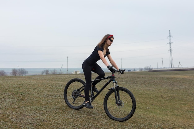 Garota em uma bicicleta de montanha em offroad belo retrato de um ciclista em tempo chuvoso Garota fitness monta uma moderna bicicleta de montanha de fibra de carbono em roupas esportivas Closeup retrato de uma garota de bandana vermelha