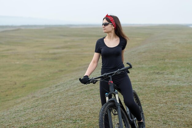 Garota em uma bicicleta de montanha em offroad belo retrato de um ciclista em tempo chuvoso Garota fitness monta uma moderna bicicleta de montanha de fibra de carbono em roupas esportivas Closeup retrato de uma garota de bandana vermelha