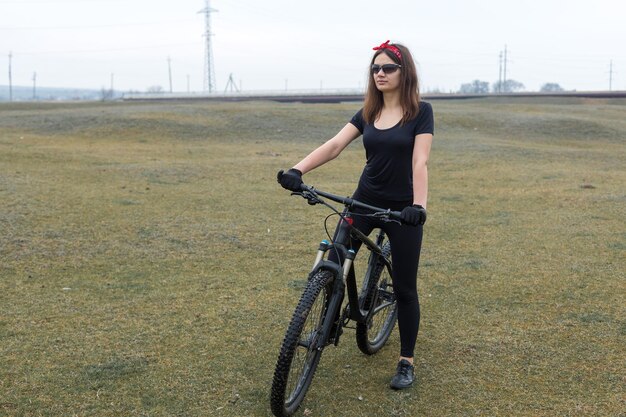 Garota em uma bicicleta de montanha em offroad belo retrato de um ciclista em tempo chuvoso garota fitness monta uma moderna bicicleta de montanha de fibra de carbono em roupas esportivas closeup retrato de uma garota de bandana vermelha