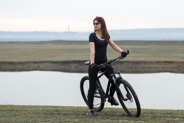 Garota em uma bicicleta de montanha em offroad belo retrato de um ciclista em tempo chuvoso garota fitness monta uma moderna bicicleta de montanha de fibra de carbono em roupas esportivas closeup retrato de uma garota de bandana vermelha