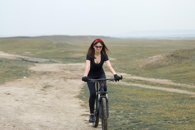 Garota em uma bicicleta de montanha em offroad belo retrato de um ciclista em tempo chuvoso Garota fitness monta uma moderna bicicleta de montanha de fibra de carbono em roupas esportivas Closeup retrato de uma garota de bandana vermelha