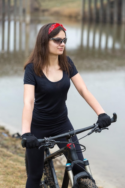 Garota em uma bicicleta de montanha em offroad belo retrato de um ciclista em tempo chuvoso Garota fitness monta uma moderna bicicleta de montanha de fibra de carbono em roupas esportivas Closeup retrato de uma garota de bandana vermelha