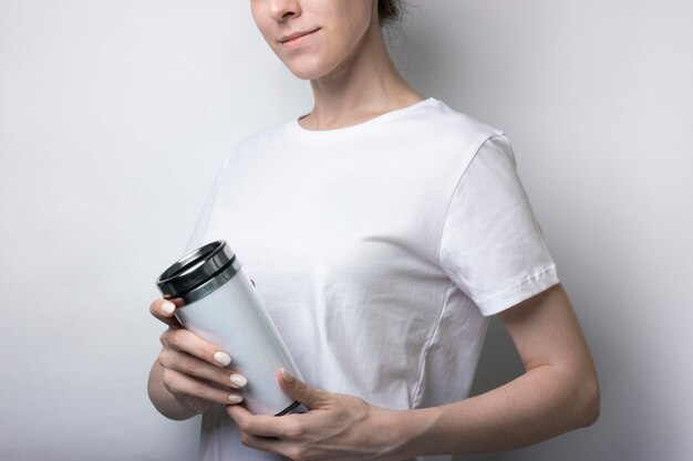 Garota em uma camiseta branca detém uma thermocup com café. em branco para a marca. maquete monocromática