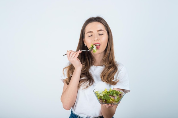 garota em uma camiseta branca tem uma tigela de salada nas mãos e come