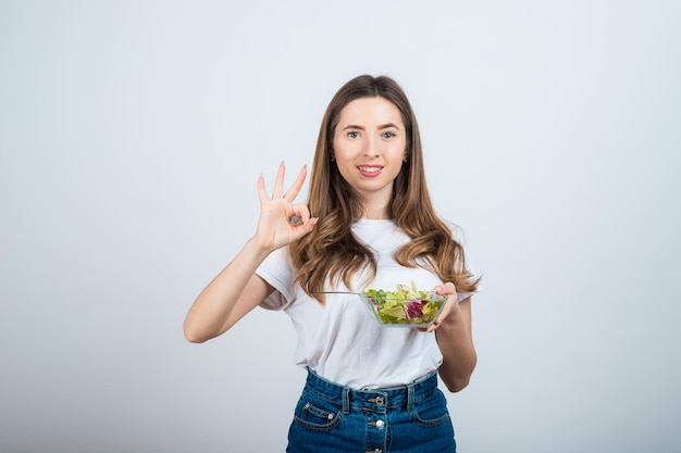 garota em uma camiseta branca tem uma tigela de salada nas mãos e come