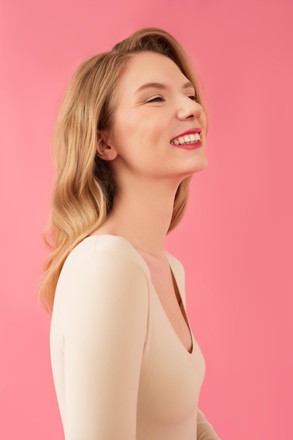 Garota em uma roupa bege com longos cabelos loiros isolados em um fundo rosa posando e sorrindo