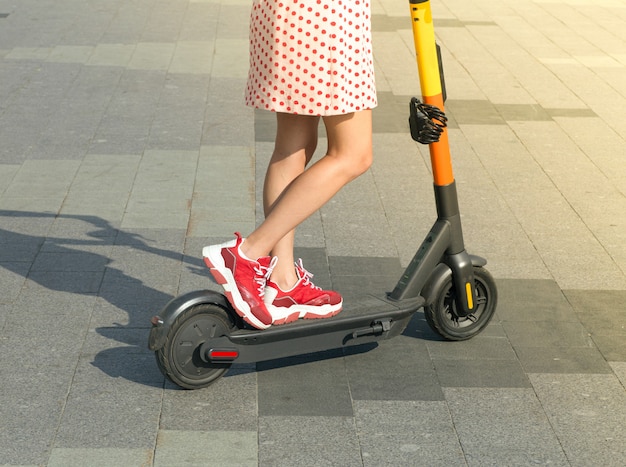 Garota em uma scooter elétrica em um dia claro de verão na cidade. Aluguel de scooter elétrico e atividades ao ar livre na cidade no verão.