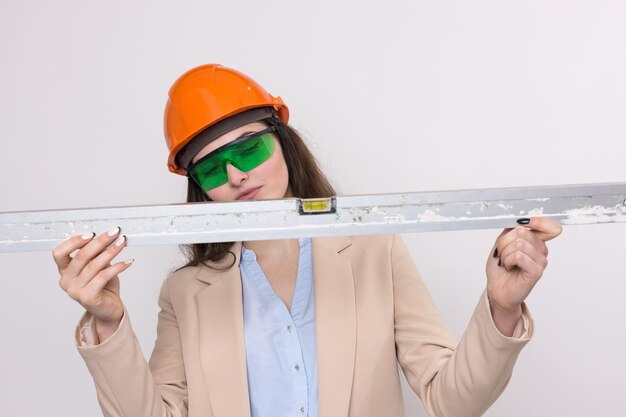 Garota engenheira em um capacete de construção laranja com um nível de construção nas mãos em um branco