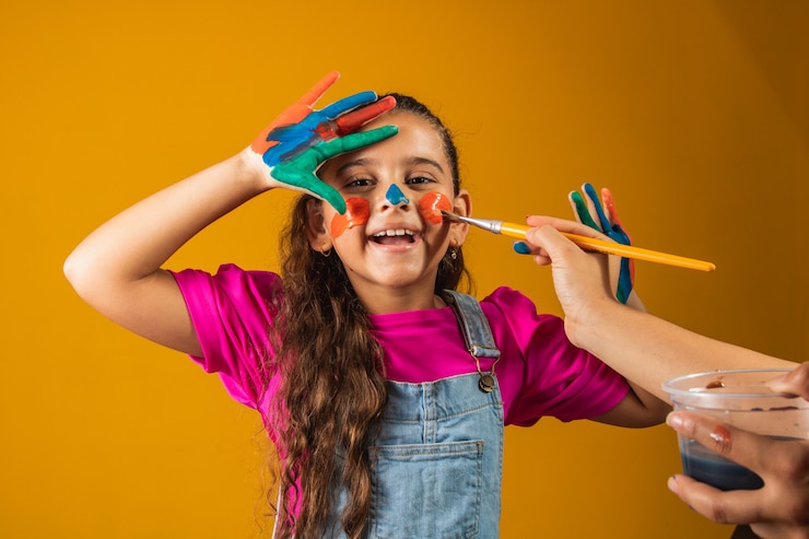 Foto garota engraçada com as mãos pintadas com tinta colorida. menina sendo pintada com tinta e pincel